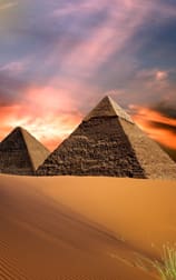 Two pyramids in the desert with a sunset behind them.