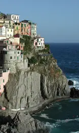 A cliff with many houses on it and the ocean in the background.