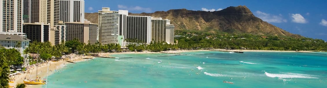 A view of the ocean and buildings in front of mountains.