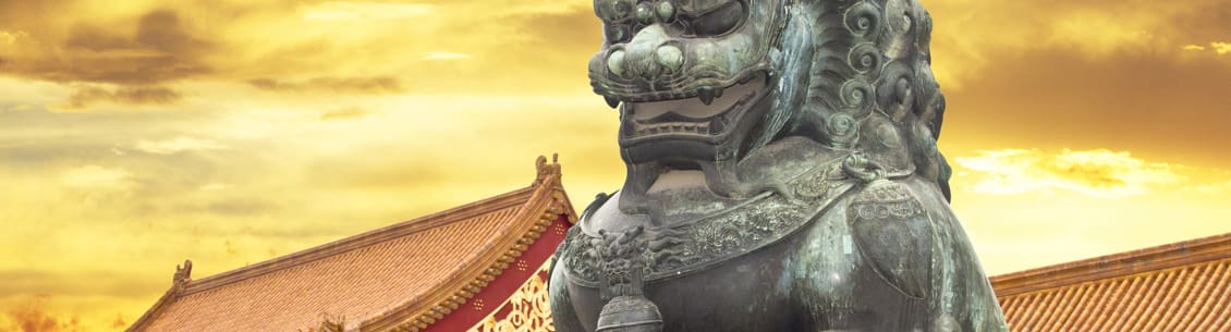 A statue of a lion with a chinese roof in the background.